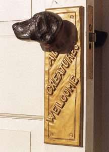 A door knob in the shape of a dogs head with "All Creatures Welcome" written underneath