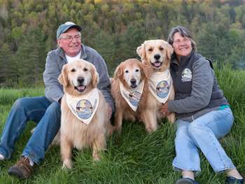 A couple and their three dogs sitting in the grass