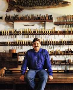 Stephen Huneck sitting on a workbench in front of carving tools in his workshop
