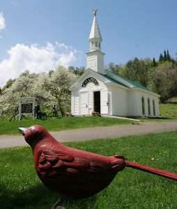 A wooden carved bird in front of Dog Mountain Chapel on a sunny day