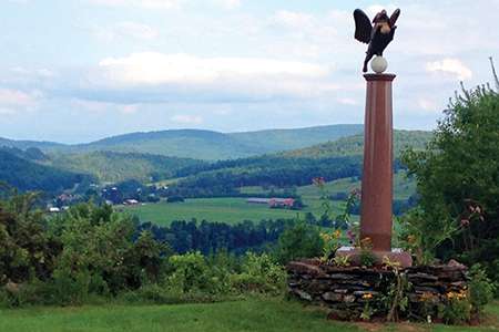 an outlook over rolling green hills with a pillar on the right side that has an angel dog statue on top of it.